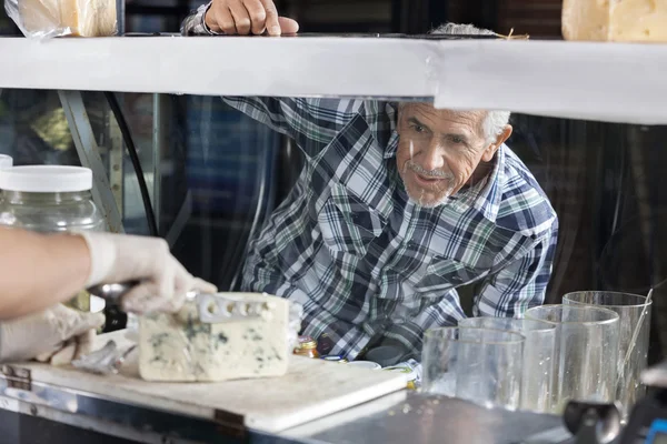 Man Watching Salesman Slicing Blue Cheese In Shop