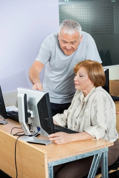 Senior Man Assisting Friend In Computer Class