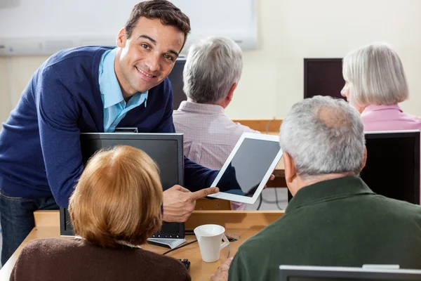 Smiling Teacher Showing Digital Tablet To Senior Students In Cla