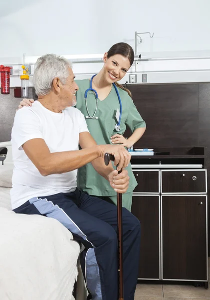 Nurse Standing By Senior On Bed In Rehab Center