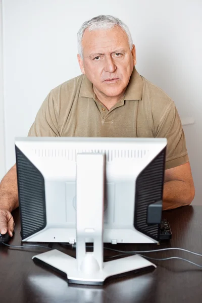 Serious Senior Man Using Computer At Desk In Class