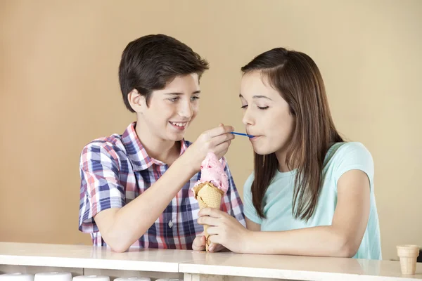 Boy Feeding Strawberry Ice Cream To Sister At Counter