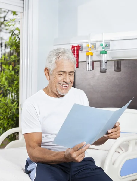 Senior Man Looking At Reports On Bed In Rehab Center