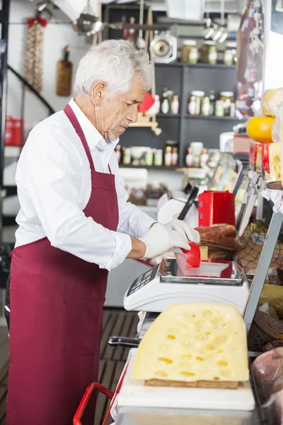 Salesman Wrapping Cheese At Counter In Shop