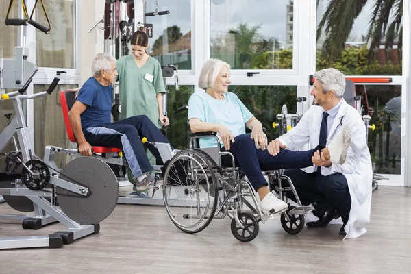 Doctor Holding Senior Womans Leg In Wheelchair At Fitness Cente