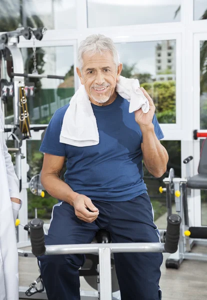 Senior Man Sitting On Exercise Bike At Rehab Fitness Center