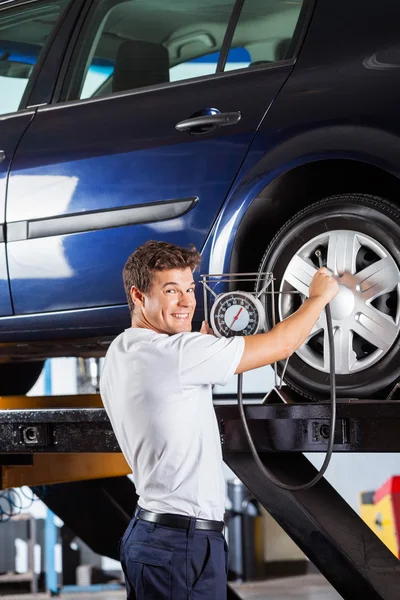 Smiling Mechanic Holding Gauge While Refilling Car Tire
