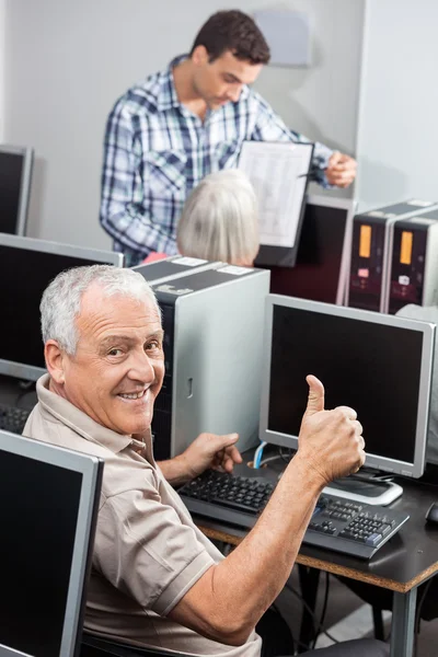 Senior Man Gesturing Thumbs Up At Computer Desk
