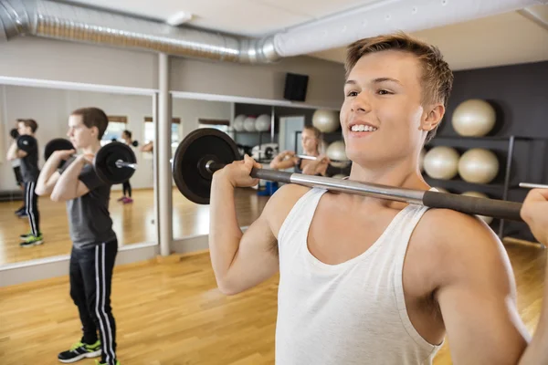 Man Lifting Barbell With Friends In Fitness Studio