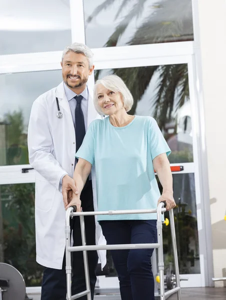 Doctor Helping Senior Female Patient With Walker In Fitness Stud