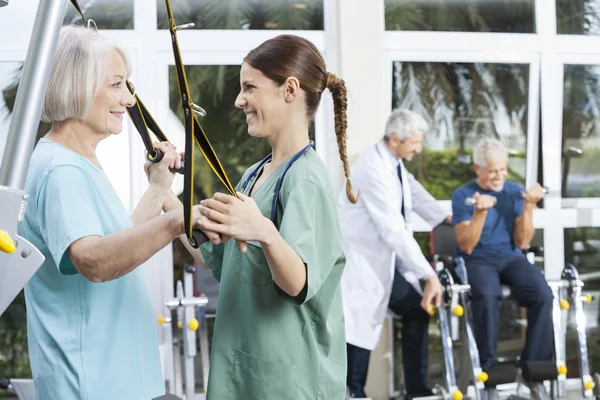 Smiling Nurse Assisting Senior Woman With Resistance Band Exerci