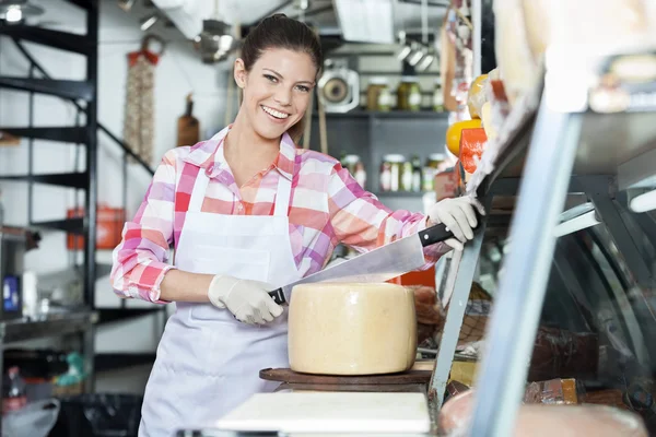 Smiling Young Saleswoman Slicing Cheese With Knife In Shop