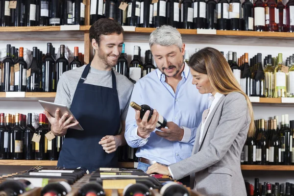 Couple With Wine Bottle Standing By Salesman Holding Digital Tab