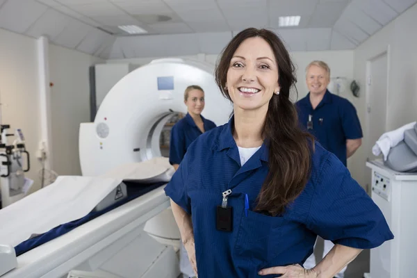 Female Radiologist With Colleagues Standing By MRI Machine