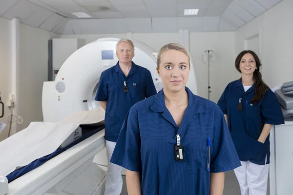 Female Doctor With Colleagues Standing By MRI Machine