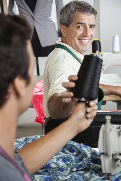 Tailor Giving Thread Spool To Colleague In Factory