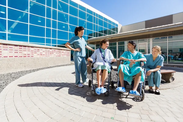Patients On Wheelchair By Nurses Outside Hospital Building