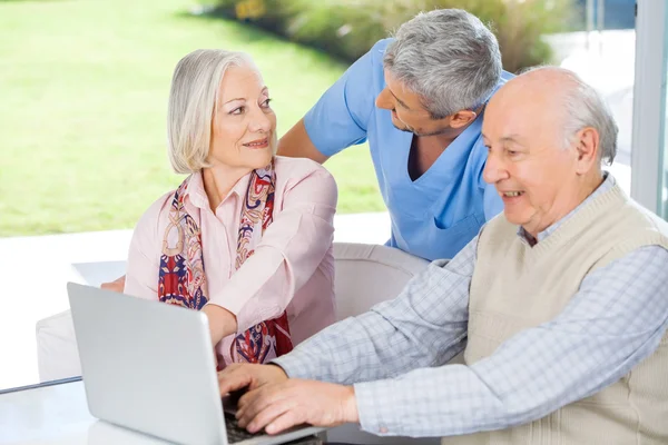 Caretaker Looking At Senior Woman By Man Using Laptop