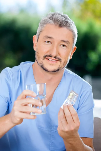 Caretaker Holding Blister Pack And Glass Of Water