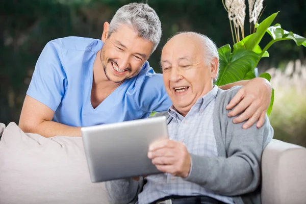 Male Nurse And Senior Man Laughing While Looking At Digital PC
