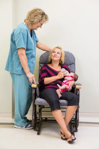 Mother Feeding Milk To Newborn Babygirl While Looking At Nurse