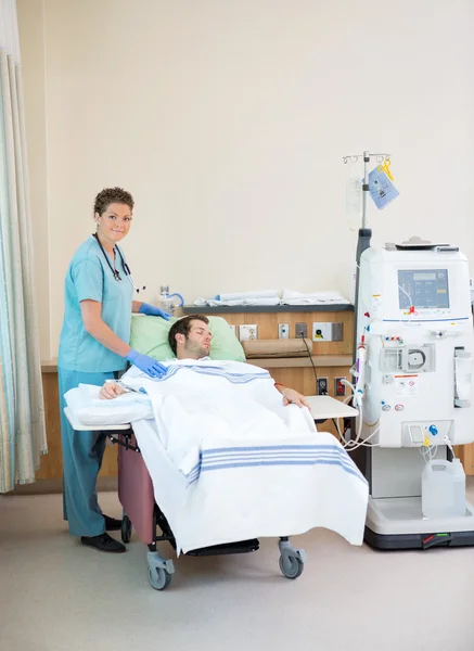 Portrait Of Nurse Standing By Patient Receiving Dialysis