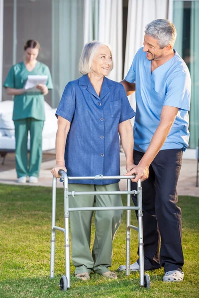 Caretaker Helping Senior Woman To Use Walking Frame