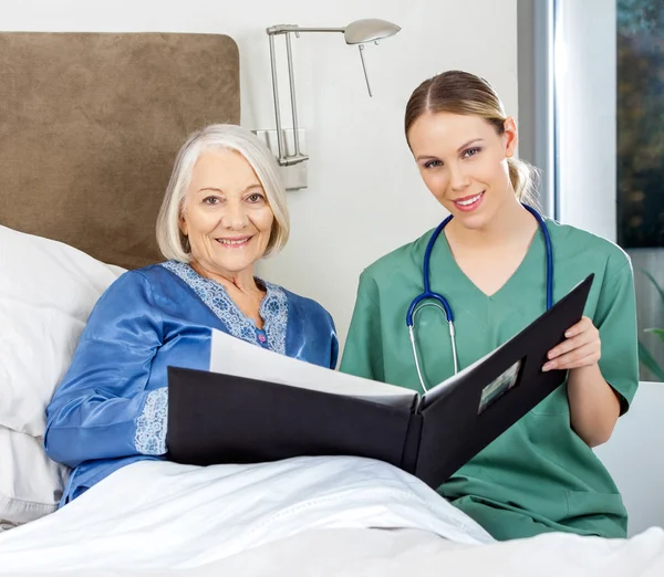 Nurse And Senior Woman With Medical Reports In Bedroom