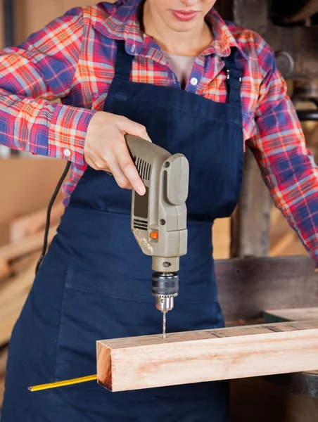 Female Carpenter Using Drill Machine On Wood