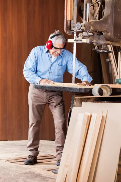 Senior Carpenter Cutting Wood With Bandsaw