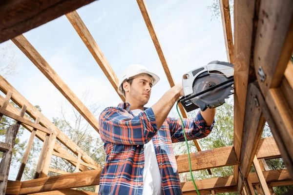 Construction Worker Using Electric Saw On Timber Frame At Site