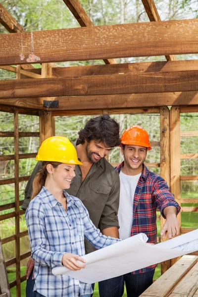 Smiling Architect Examining Blueprint With Colleagues At Site