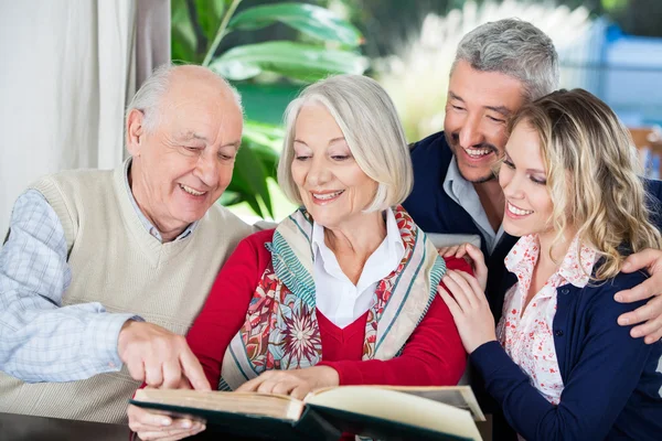 Happy Grandchildren With Grandparents Reading Book In Nursing Ho