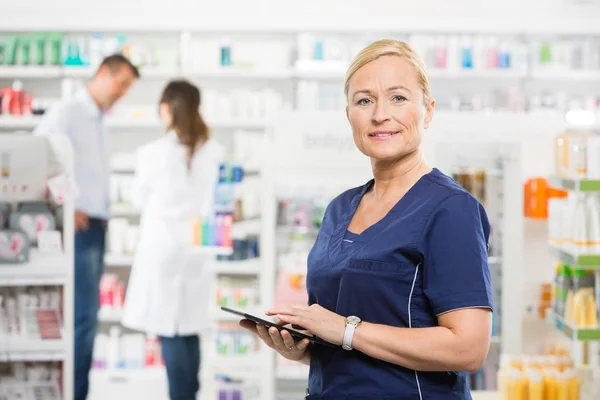Confident Assistant Holding Tablet Computer At Pharmacy