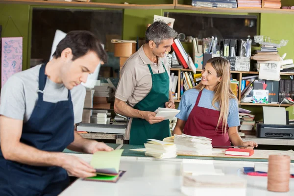 Workers Making Notebooks With Colleague In Foreground