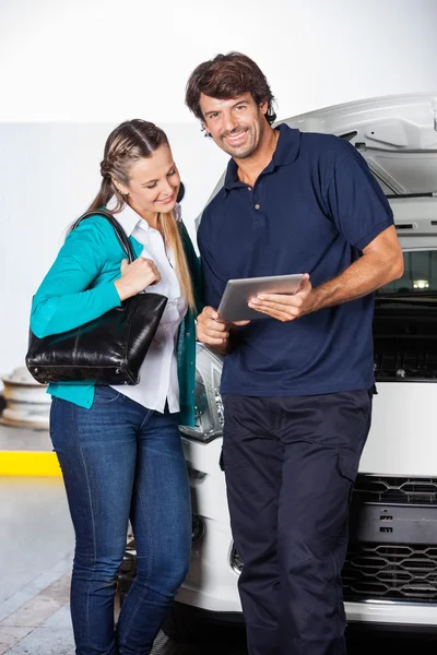 Mechanic Holding Digital Tablet While Standing With Customer