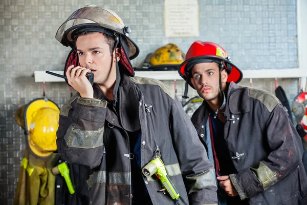 Male Firefighter Using Walkie Talkie With Colleague In Backgroun