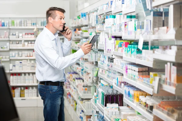 Male Customer Using Mobile Phone And Digital Tablet In Pharmacy