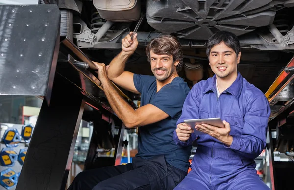 Mechanics With Digital Tablet Working Under Lifted Car