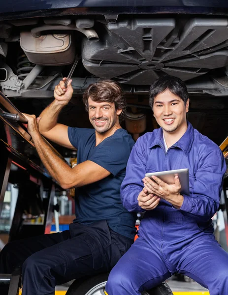 Mechanics With Tablet Computer Sitting Under Lifted Car