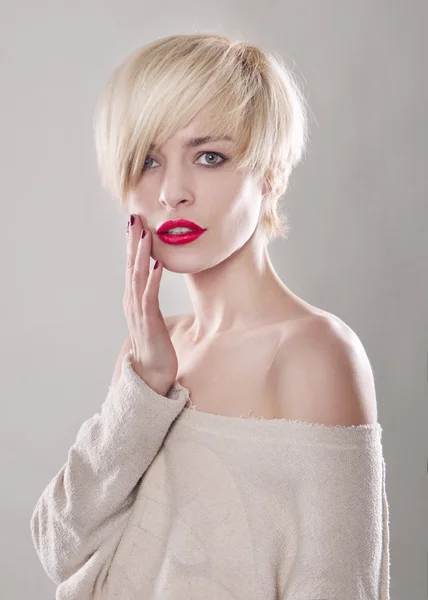 The blond woman with short hair and a beautiful smile with red lips isolated. Touches the lips