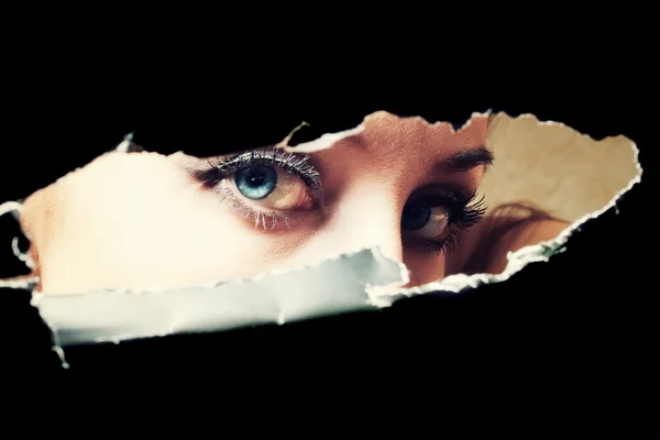 Blue eyes of young woman peeping through a hole