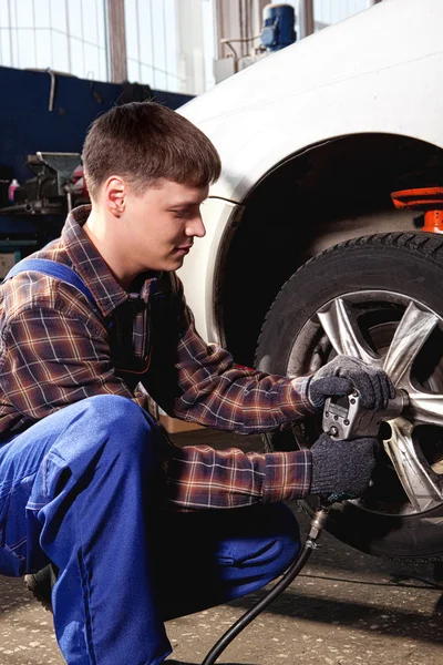 Car mechanic screwing or unscrewing car wheel of lifted automobi