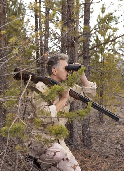 Hunter with shotgun looking through binoculars