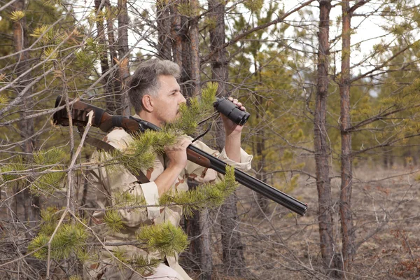 Hunter with shotgun looking through binoculars