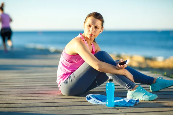 Woman resting after jogging on a wooden path at the sea