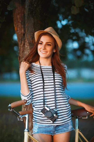 Lovely young woman in a hat with a bicycle in a park