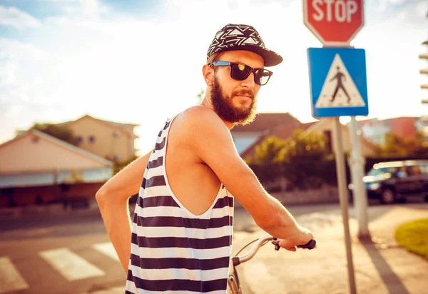 Young man in sunglasses riding a bicycle on a city street at sun