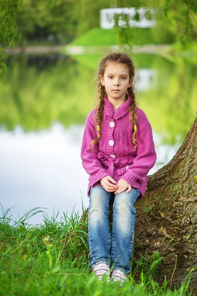 Little girl sits near lake