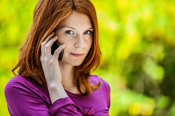 Red-haired smiling young woman talking on phone